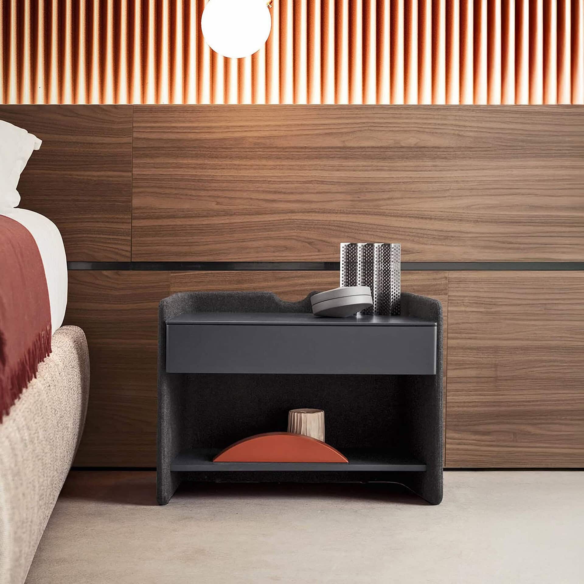 Bedroom setting with the Chloé Upholstered Nightstand placed beside a bed and wooden paneled wall, styled with decor for a modern look.