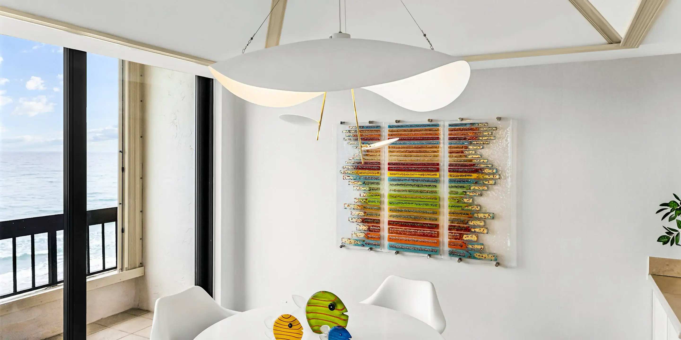 Modern coastal living room with ocean view and colorful wall art Modern coastal living room with ocean view, white furniture, and vibrant abstract wall art.