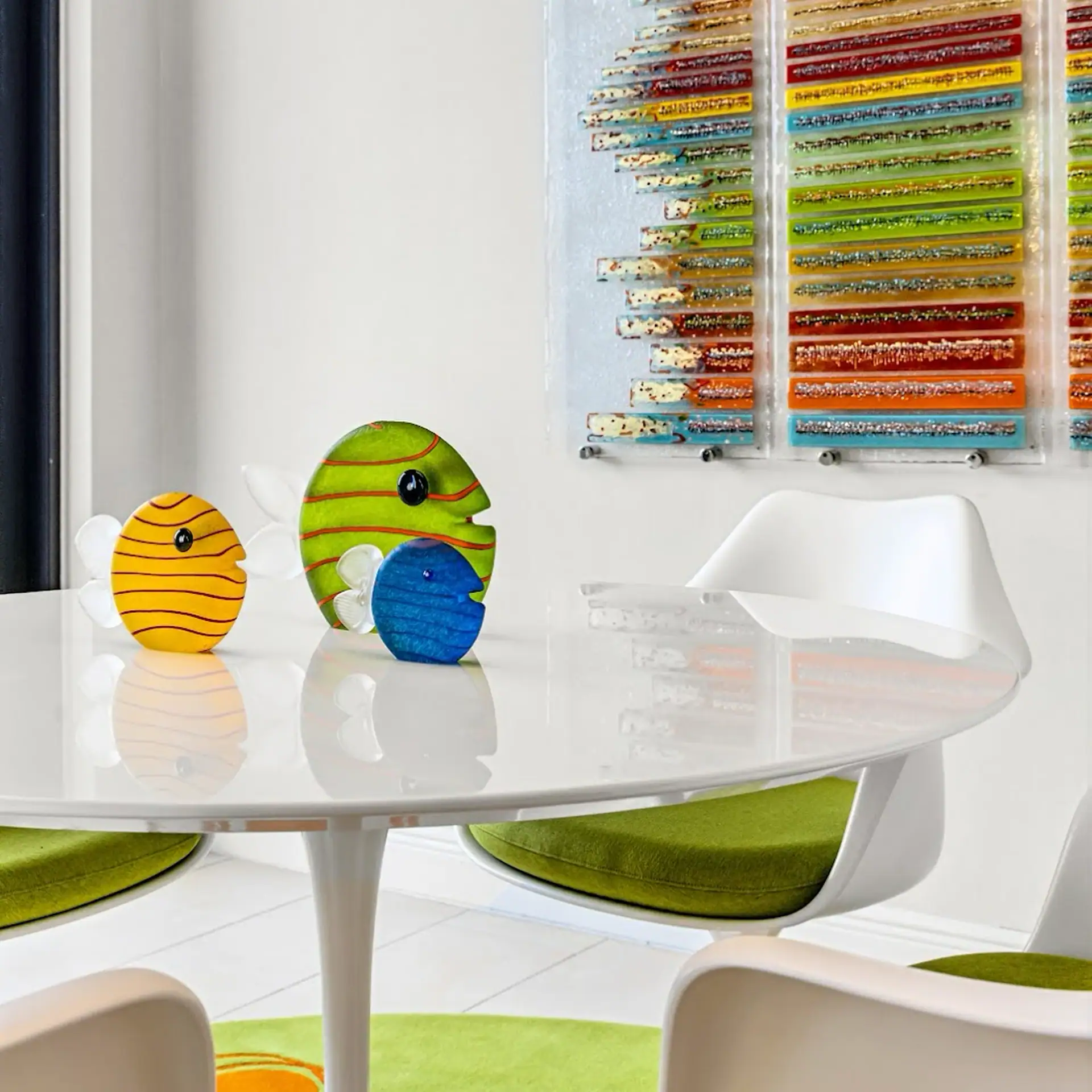 Playful fish-shaped decor on a modern dining table with colorful art in the background Bright fish-shaped decor pieces on a sleek white dining table with colorful artwork in the backgroun.