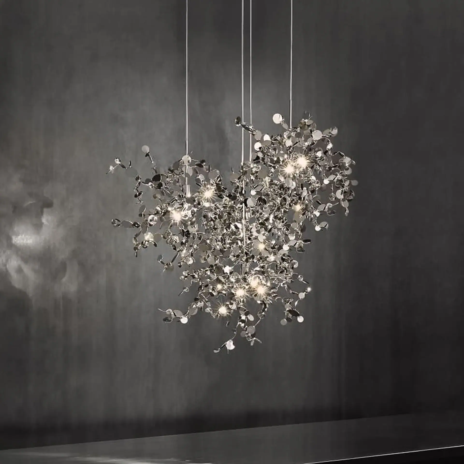 A modern, metallic chandelier with multiple lights and reflective discs hangs against a dark gray wall.