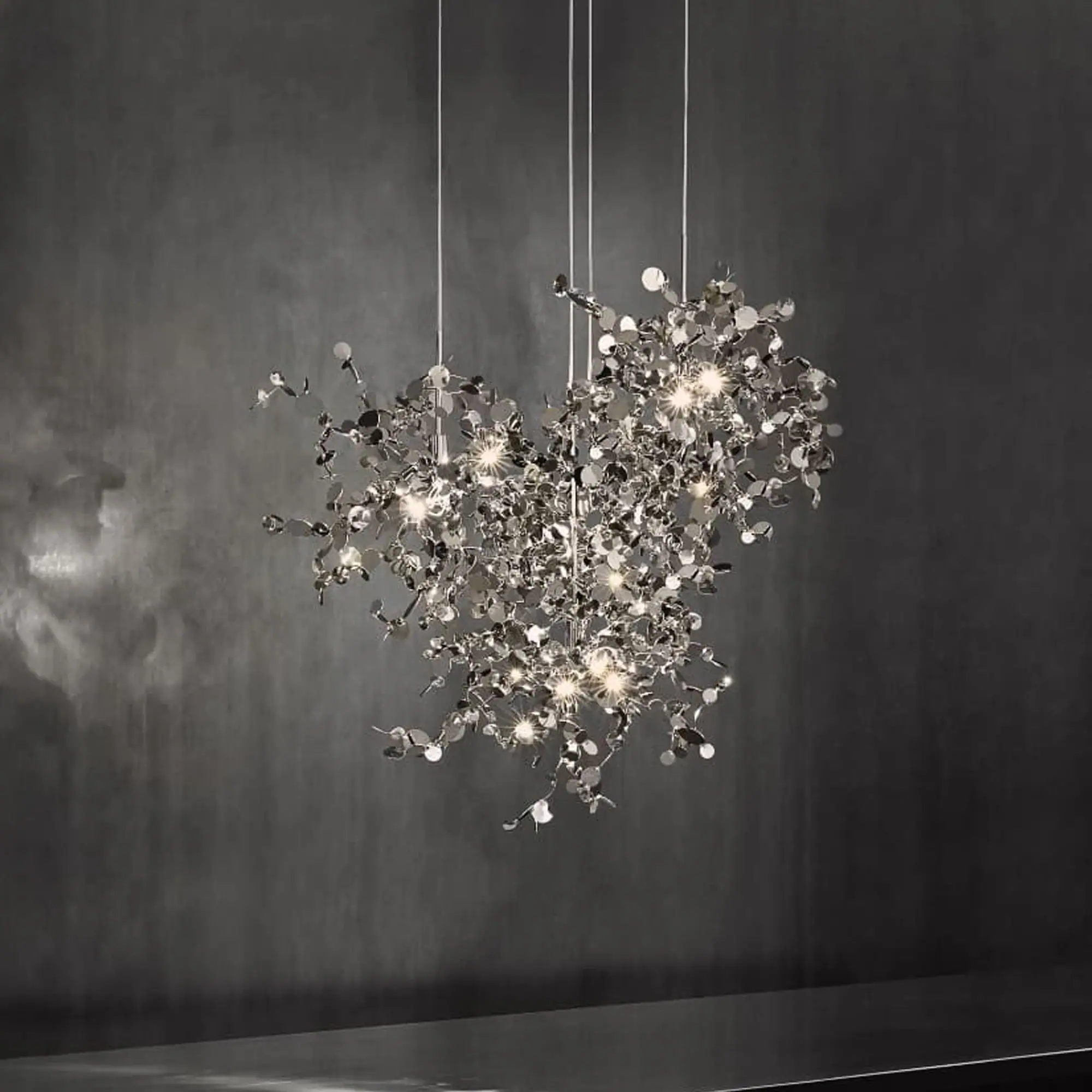 A modern, metallic chandelier with multiple lights and reflective discs hangs against a dark gray wall.