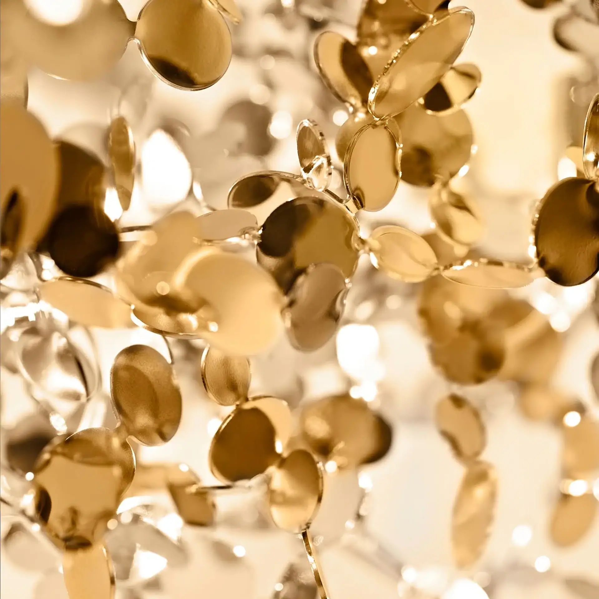 Close-up of numerous golden, reflective, disc-like shapes, some in focus, others blurred, creating a shimmering effect.