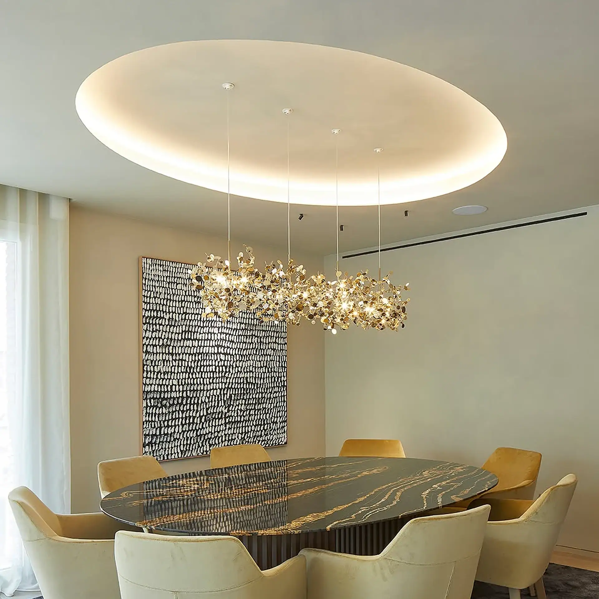 A modern dining room with an oval black marble table, cream chairs, and a golden leaf-motif chandelier above, with abstract art on the wall.