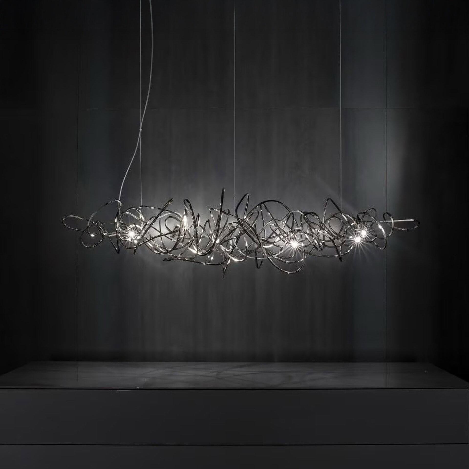 Terzani Doodle Linear Chandelier suspended in a dark modern interior, showcasing free-form brass loops with integrated LED lights.