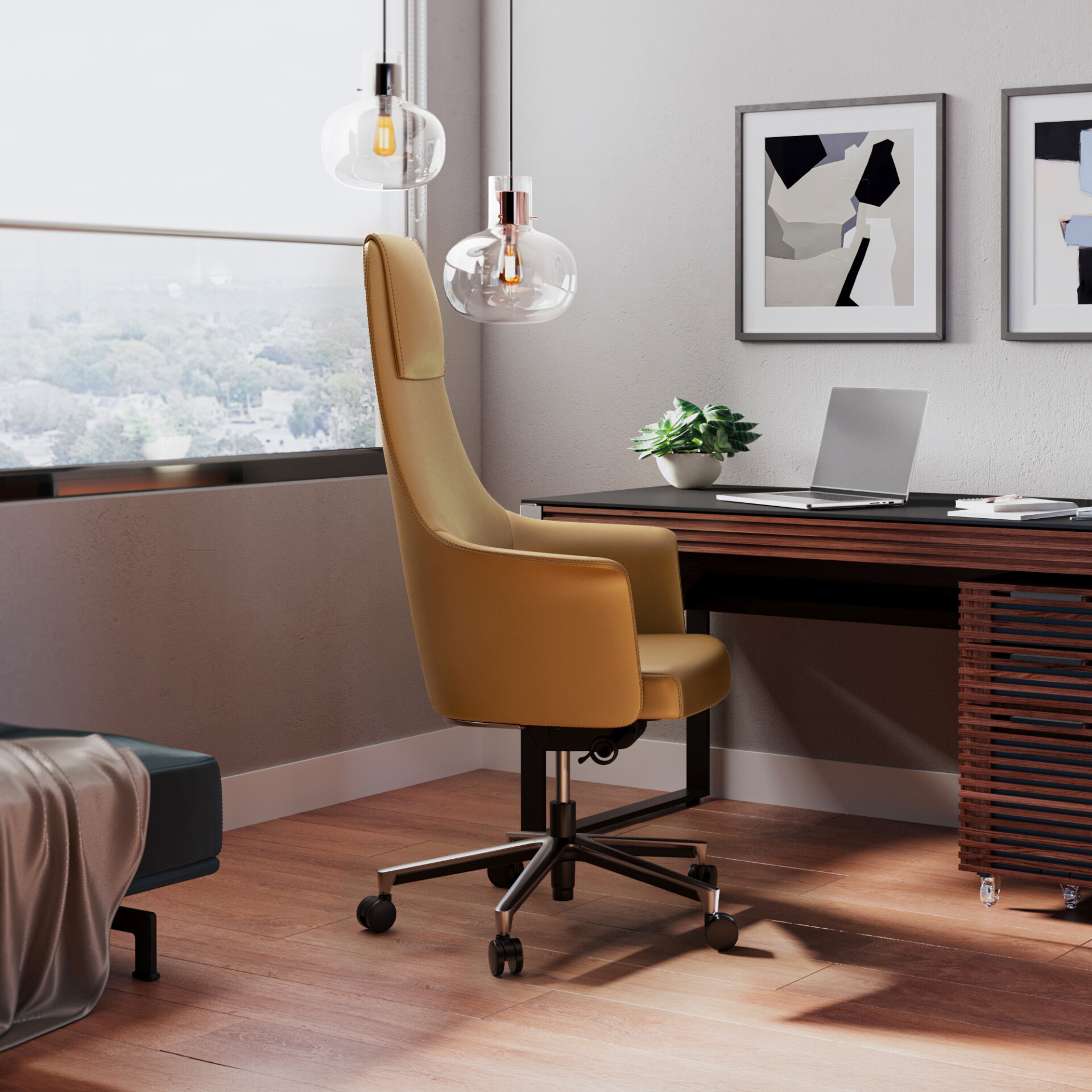 A modern home office with a mustard-colored ergonomic chair, a dark wooden desk with a laptop and plant, and two abstract art pieces on a light gray wall. Natural light streams in from a large window, illuminating the wooden floor.