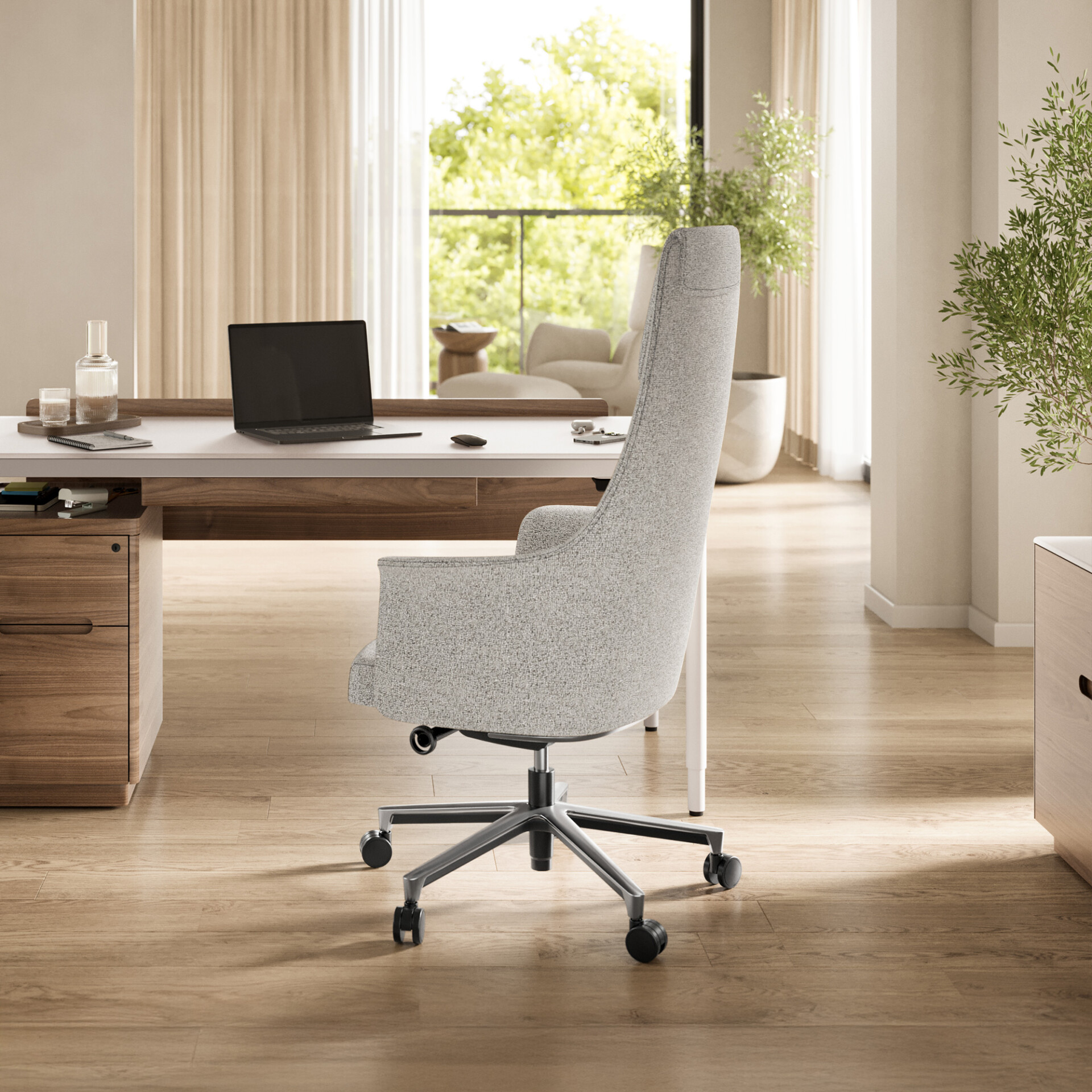 A modern home office featuring a light grey ergonomic chair, a white and wood desk with a laptop, and a large window overlooking green trees and a balcony.