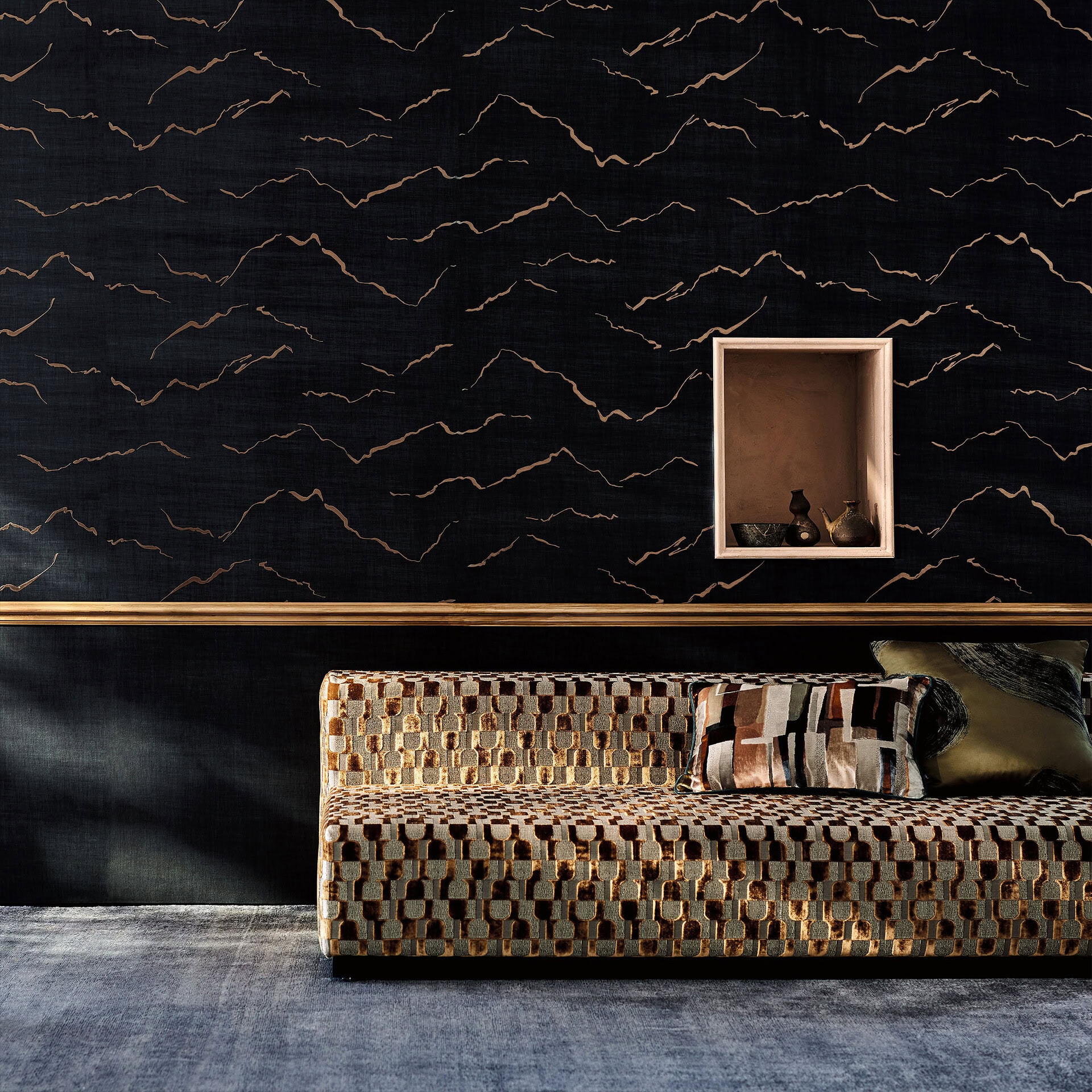 Living room with Kuju Textured Metallic Wallpaper in Shadow, featuring deep charcoal tones with flowing metallic lines, styled with a patterned sofa and wall niche accent.