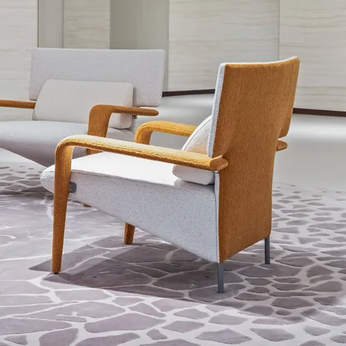 Two modern armchairs with curved armrests on a patterned rug. The foreground chair has a light gray seat and back, with mustard yellow armrests and back. The background chair is similar, with lighter armrests.