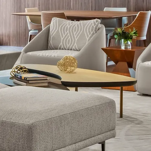 A modern living room with a grey armchair, an irregular coffee table with golden decor, and a wooden dining table in the background.