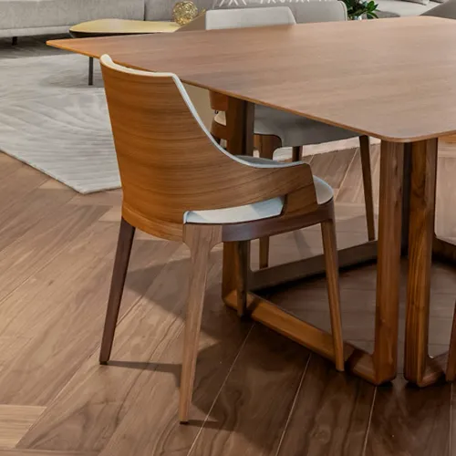 A modern wooden dining table and a curved wooden chair with a light upholstered seat in a contemporary dining room with wooden floors.