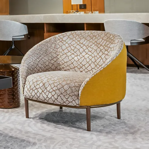 A modern barrel armchair with a cream and gold geometric patterned interior and a solid mustard yellow velvet exterior, on a light patterned carpet in a lounge setting.