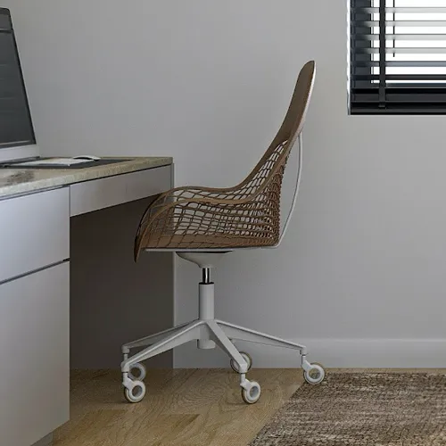 A modern office chair with a woven brown seat and white base sits next to a light gray desk with a computer monitor. The room has light walls, a wooden floor, a textured rug, and a window with black blinds.