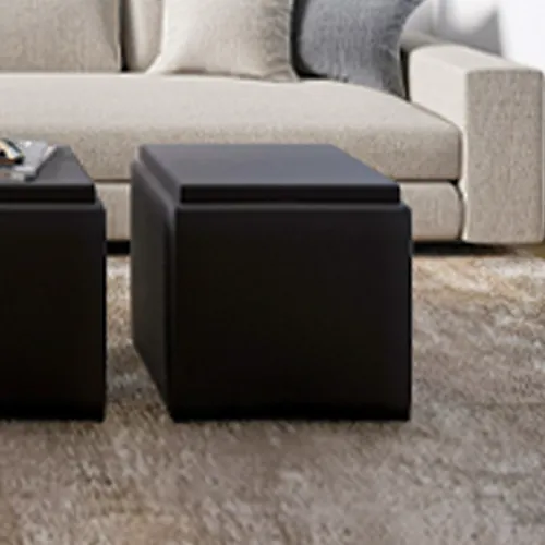 Two dark square ottomans in a modern living room with a light beige sofa and a textured rug.