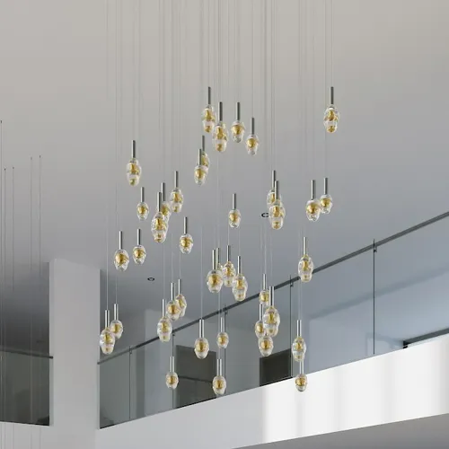 A large, modern chandelier with numerous clear, teardrop-shaped pendant lights, each with a golden interior, hangs at varying heights in a high-ceilinged, minimalist interior with a glass railing.