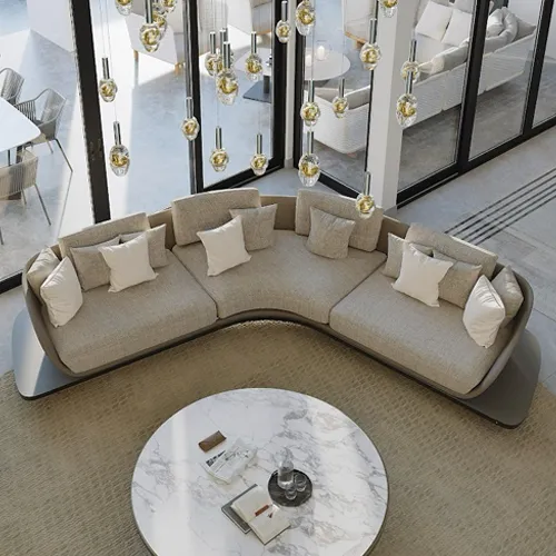 High-angle view of a modern living room featuring a large, curved beige sectional sofa, a round white marble coffee table, and numerous hanging glass pendant lights. Large windows are visible in the background.