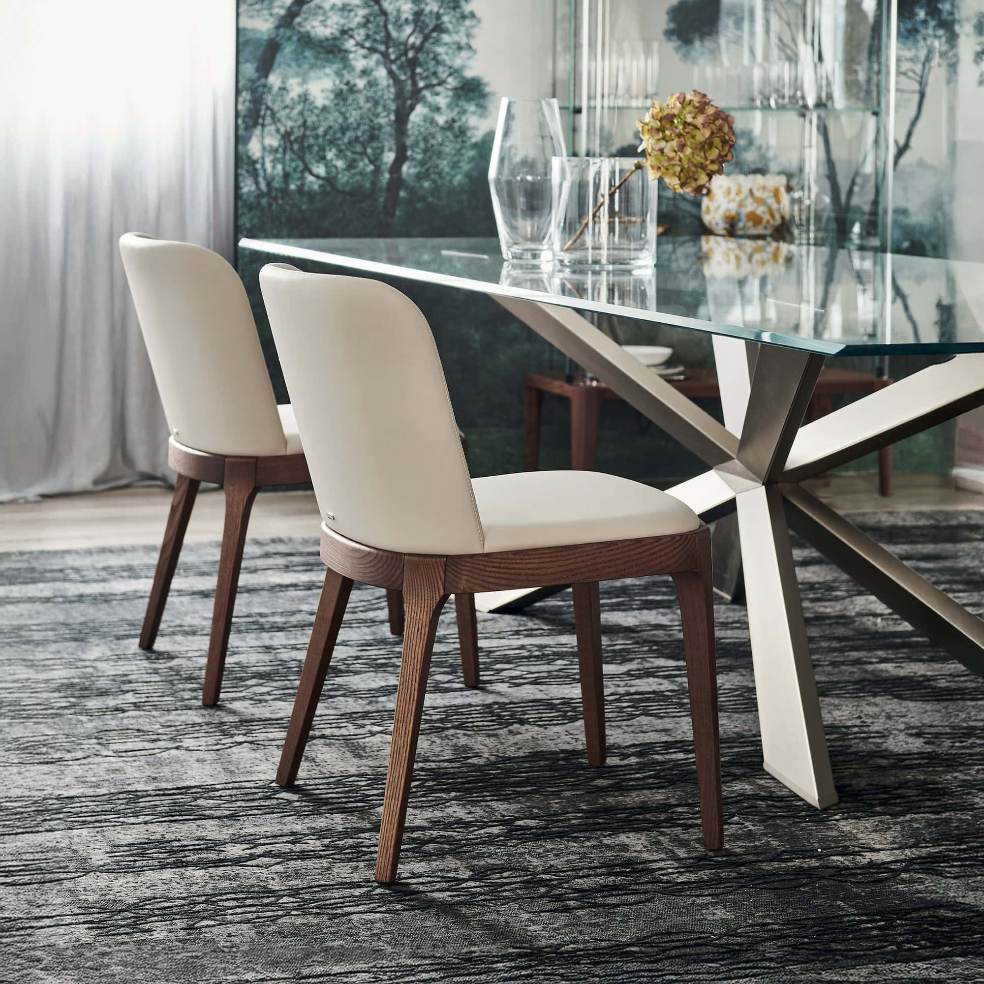 Contemporary glass-top dining table with cream and wood upholstered chairs in modern interior setting.