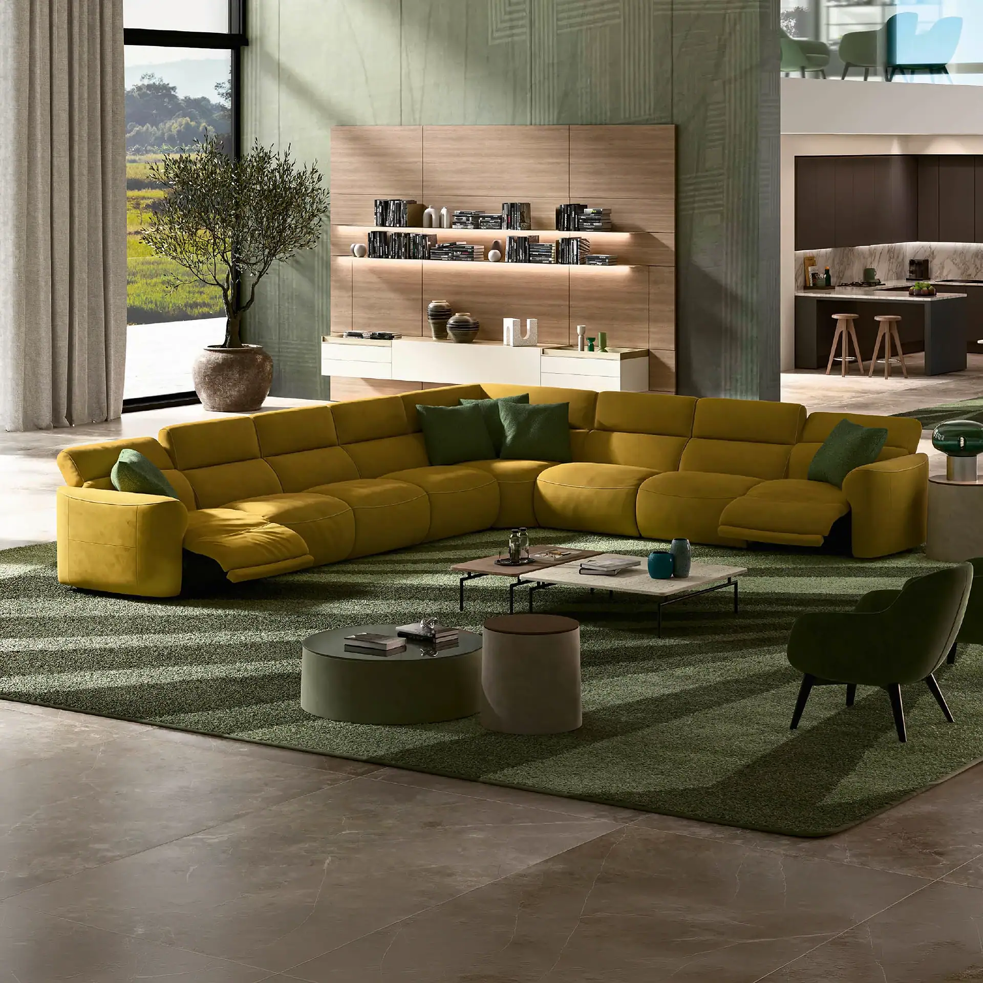 A modern living room with a large yellow sectional sofa, green rug, wooden wall unit, and a view of green hills through a large window.