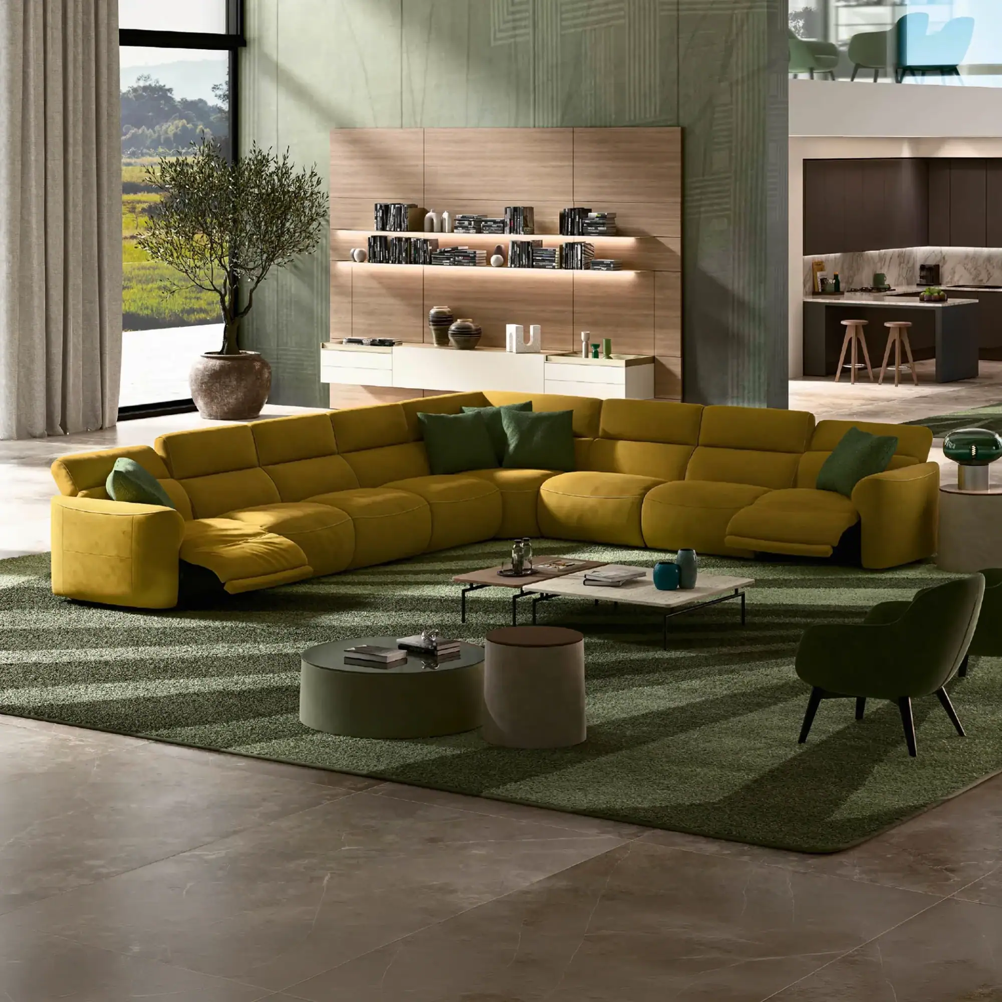 A modern living room with a large yellow sectional sofa, green rug, wooden wall unit, and a view of green hills through a large window.