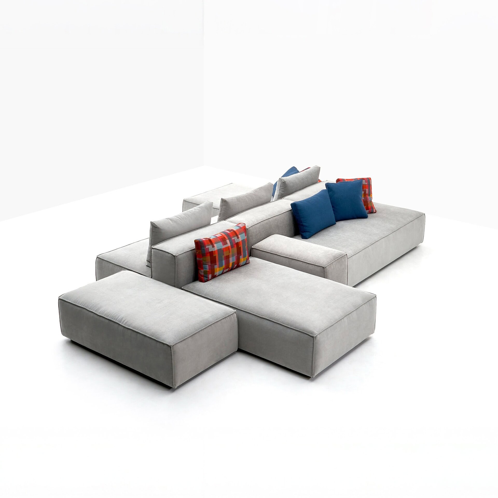 Contemporary modular layout of the Alex Seating System in gray upholstery, arranged with ottomans and colorful accent pillows on a white background.