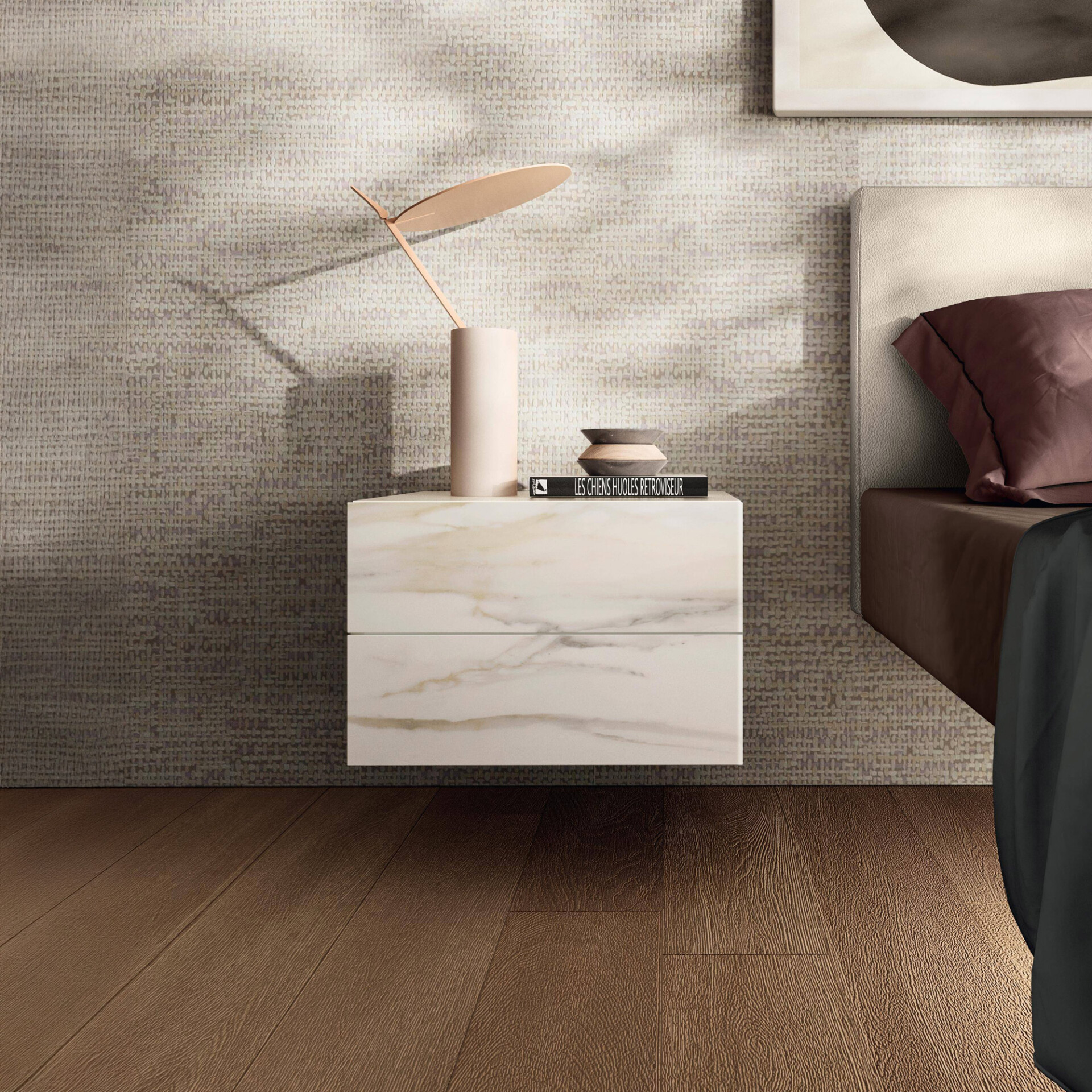 A modern bedroom scene featuring a floating white marble nightstand with gold veining. On the nightstand are a pale pink vase with a leaf-like sculpture, and decorative bowls on a book. A textured beige wall, cream headboard, and dark wood floor complete the luxurious look.