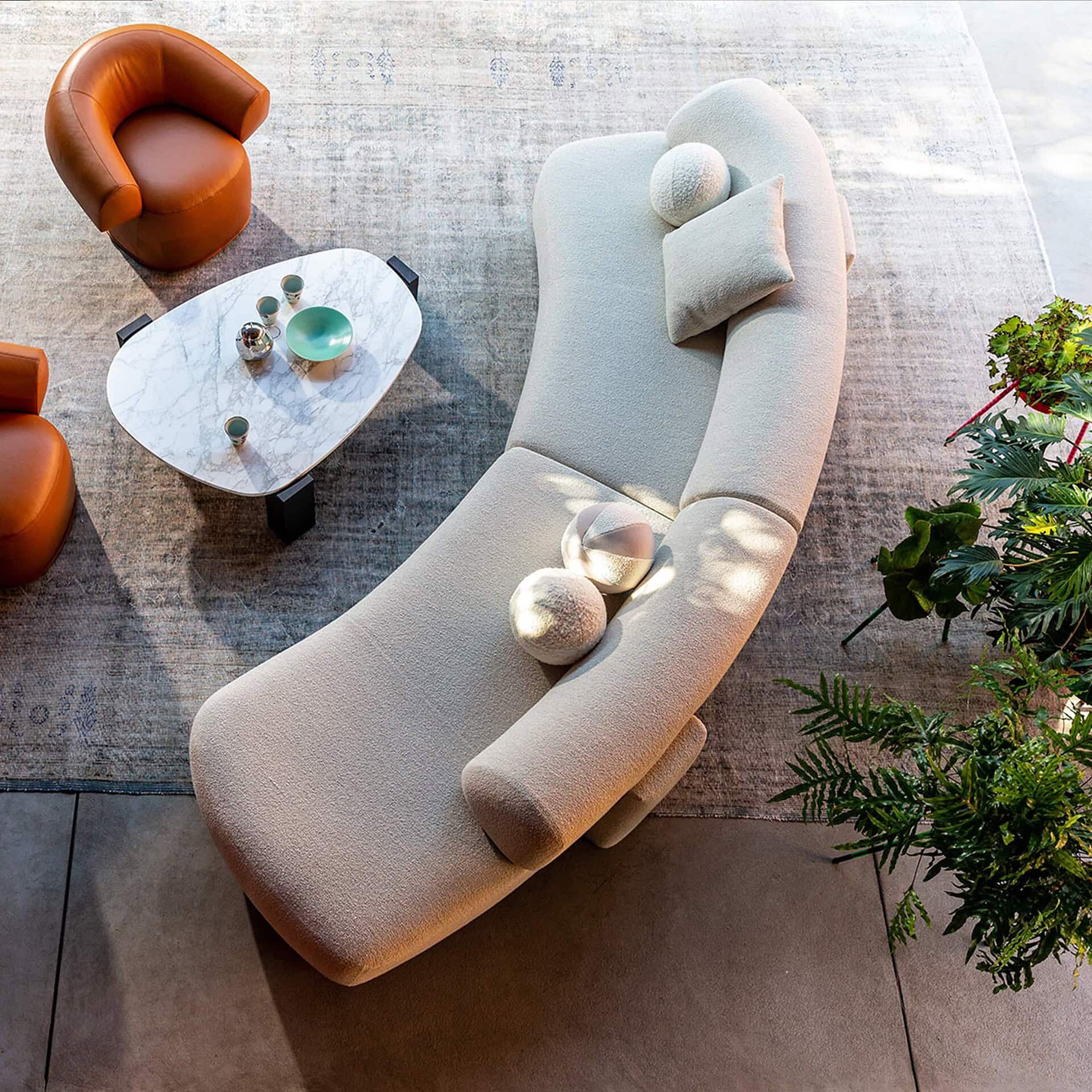Overhead view of the Gogan Modular Curved Sofa in a soft grey finish, styled with side tables and greenery.
