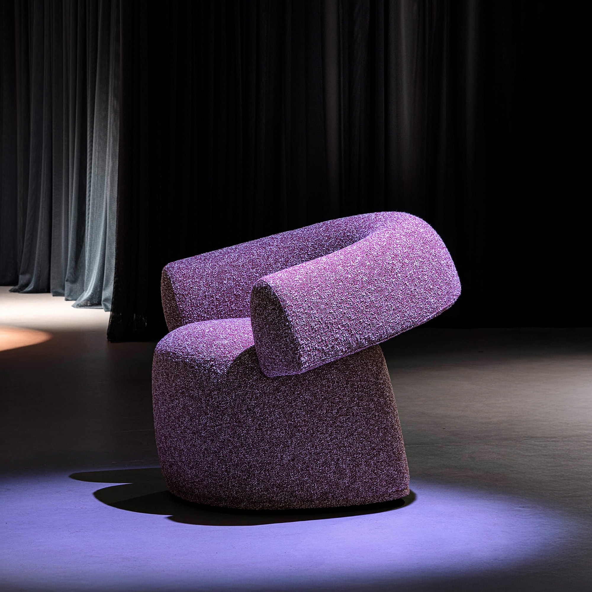 Ruff Armchair in purple fabric, spotlight studio shot with dark background.