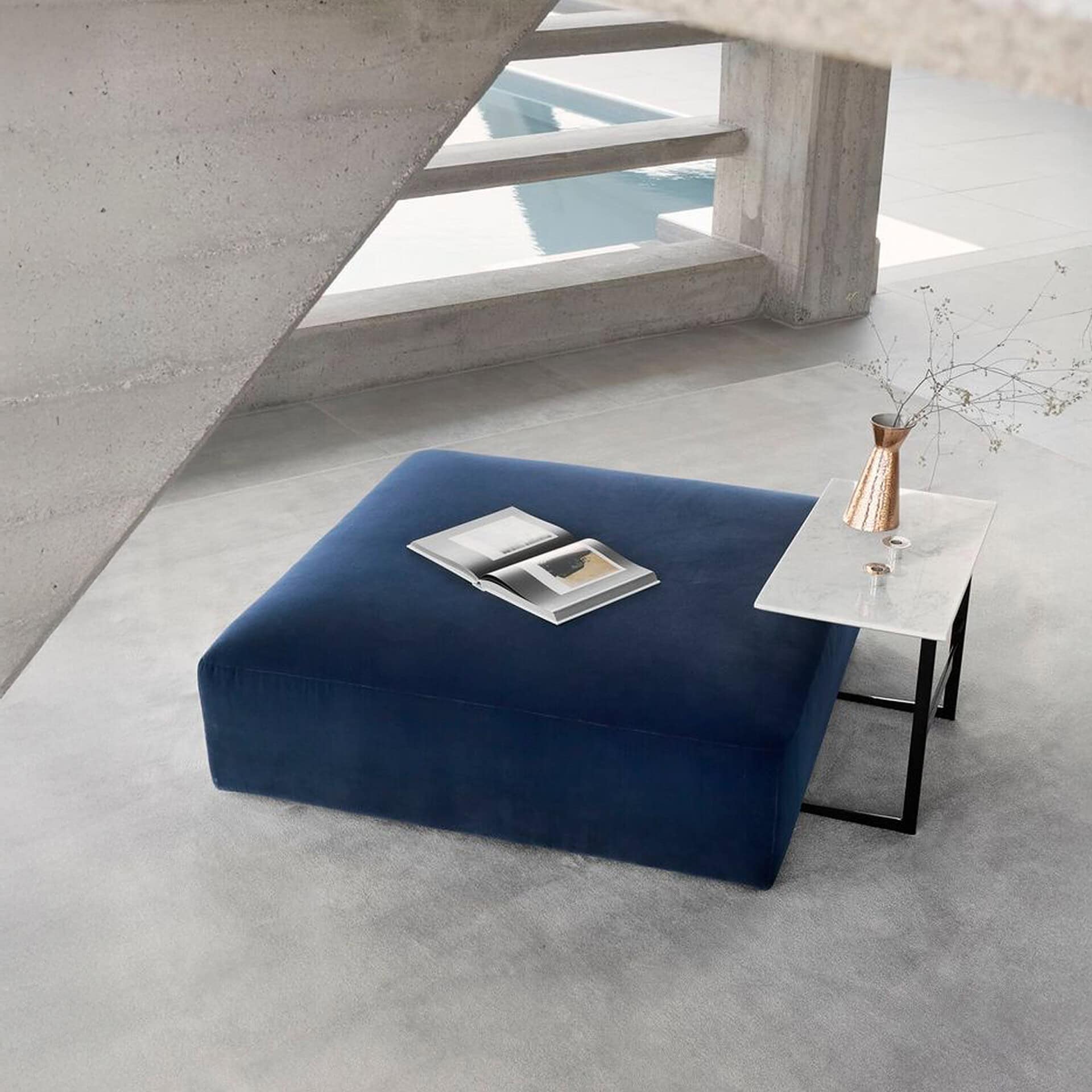 Main Square Ottoman in deep blue fabric, styled with a marble side table and decorative accents in a modern living space.