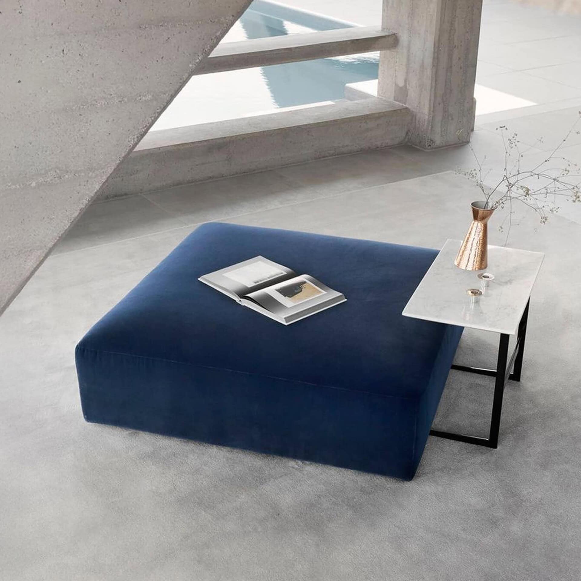 Main Square Ottoman in deep blue fabric, styled with a marble side table and decorative accents in a modern living space.