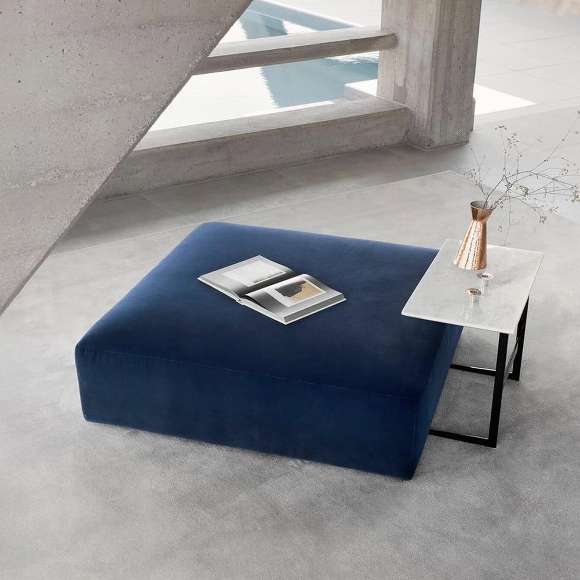 Main Square Ottoman in deep blue fabric, styled with a marble side table and decorative accents in a modern living space.