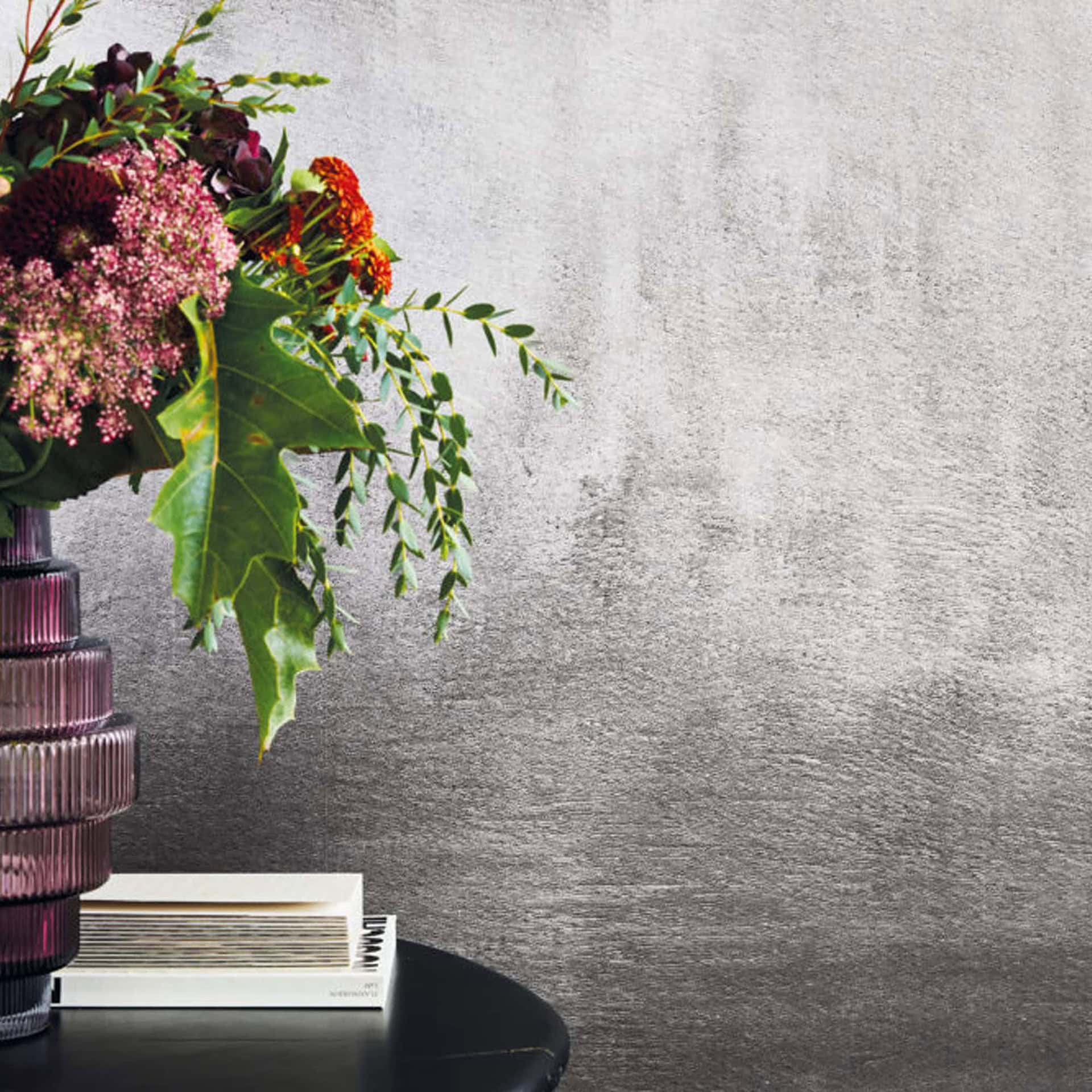 Evening Glow Metallic Wallpaper in silver finish, styled in a modern room with floral arrangement and stacked books.