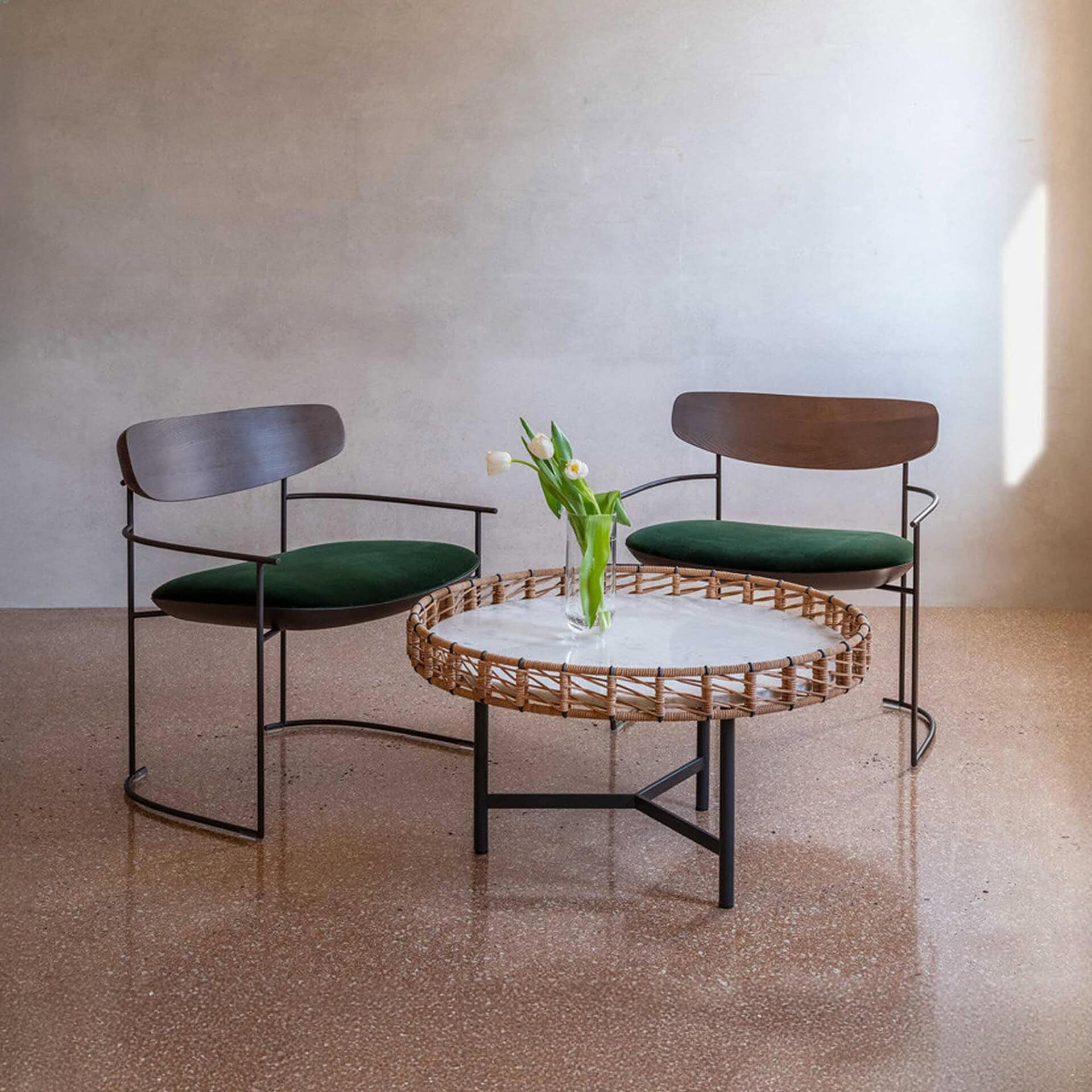 Round Ropu Woven Coffee Table with light surface, decorated with a vase of tulips and paired with two contemporary wooden chairs.