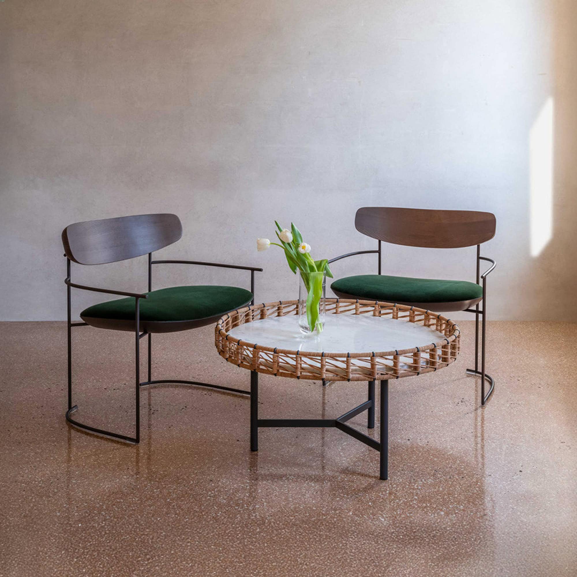 Round Ropu Woven Coffee Table with light surface, decorated with a vase of tulips and paired with two contemporary wooden chairs.