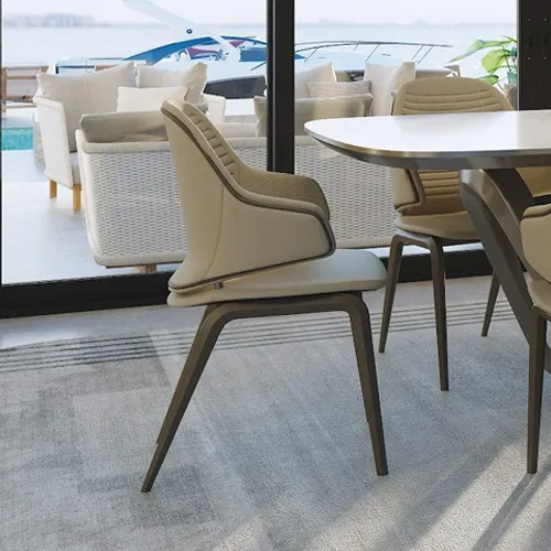 A modern dining chair with a curved beige backrest and dark legs, positioned in front of large windows overlooking a yacht on the water and outdoor patio furniture.