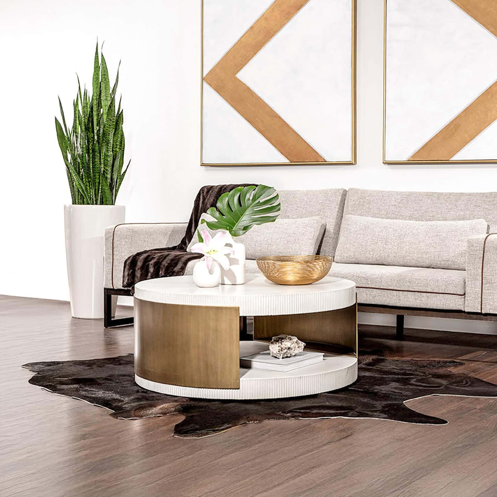 Cavette Round Concrete Coffee Table with white concrete top and antique brass base, styled with decorative accents beside a grey sofa.