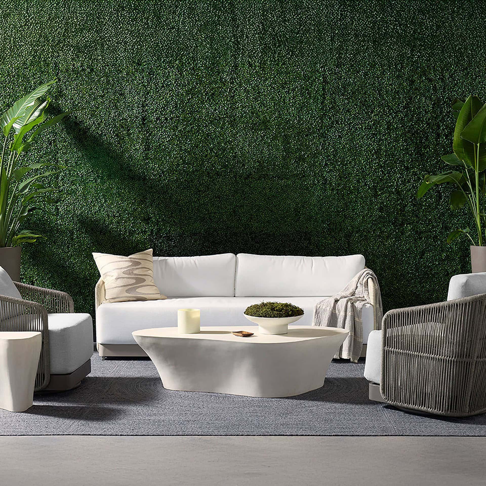 Modern outdoor lounge with the Dali Sculptural Concrete Coffee Table in white concrete, set against a green living wall backdrop.