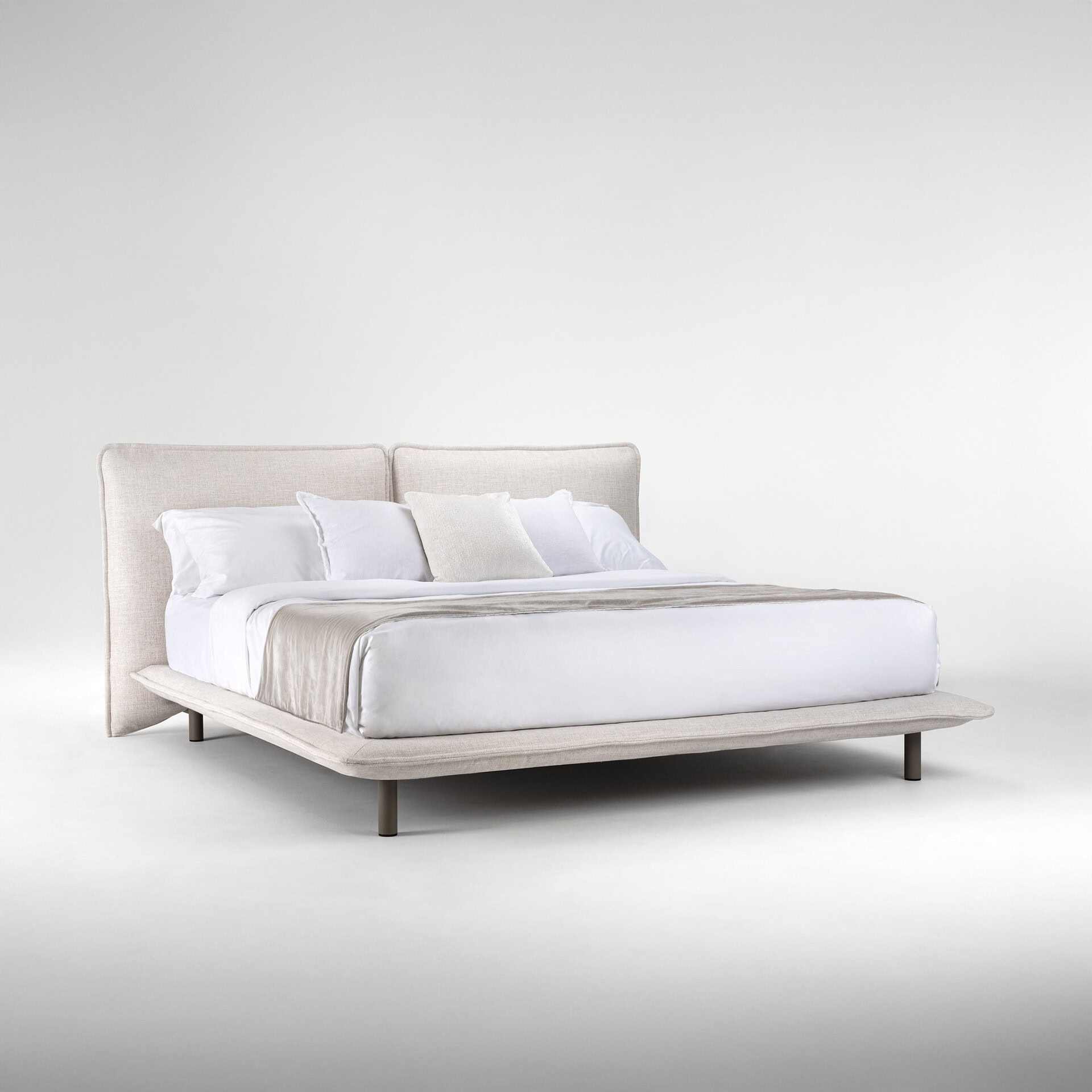 Luxurious white upholstered bed with a beige throw and multiple pillows, perfect for stylish bedroom interiors.
