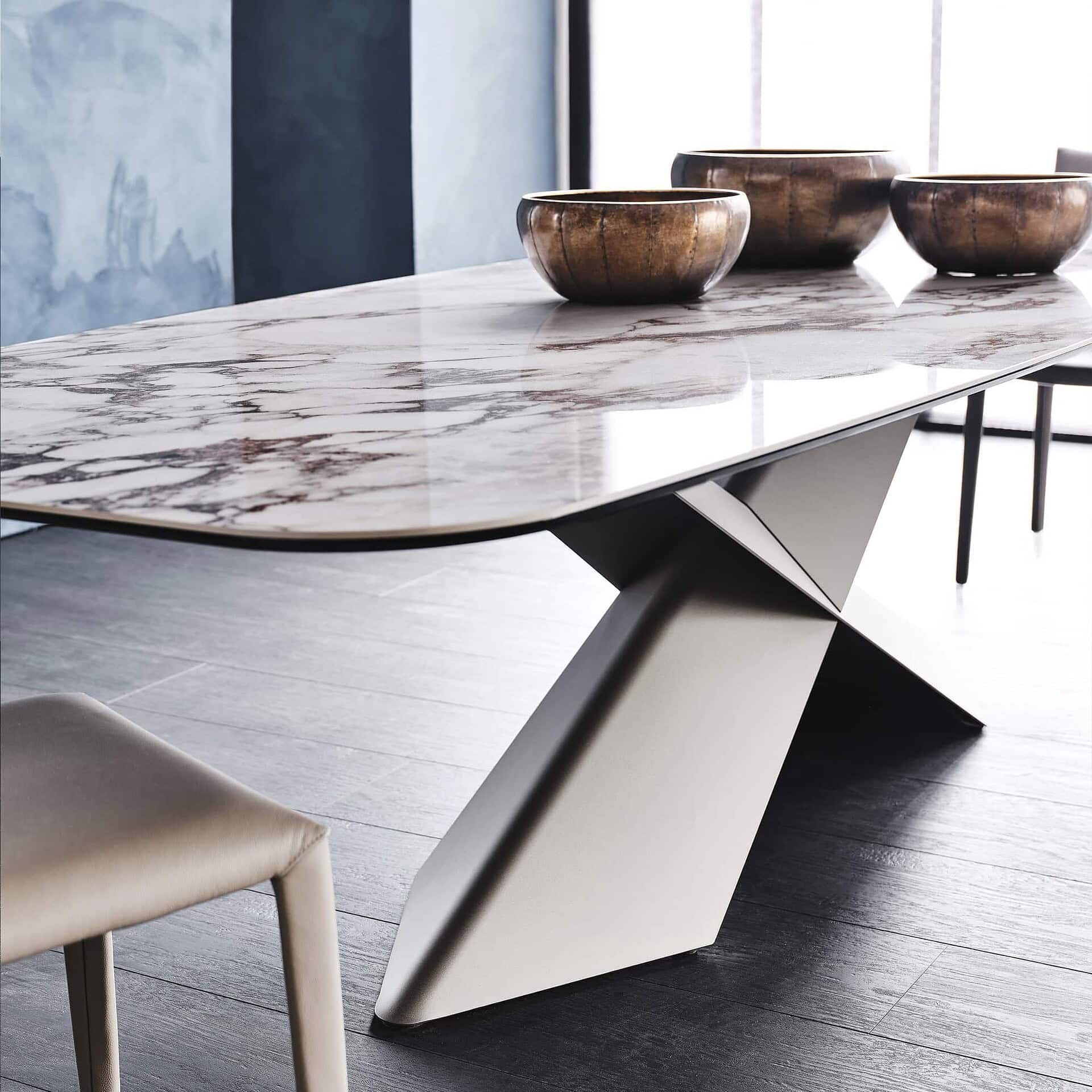 Contemporary marble dining table with modern geometric base and decorative bowls.