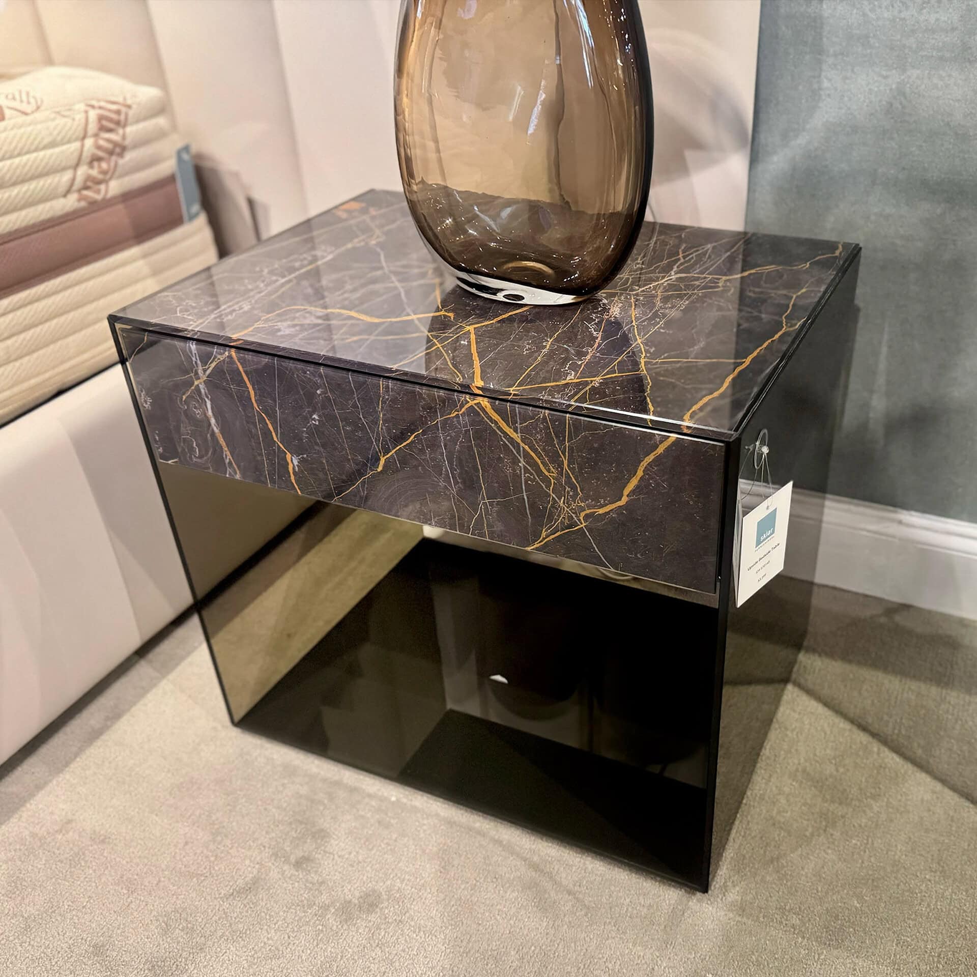 Black and gold marble nightstand with sleek glass legs for contemporary bedroom decor.