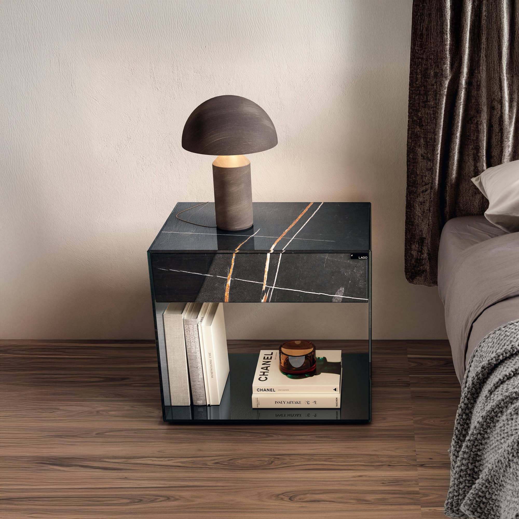 Lago UpGlass Bedside Table with transparent smoked glass design, styled beside a bed with a modern lamp on top.