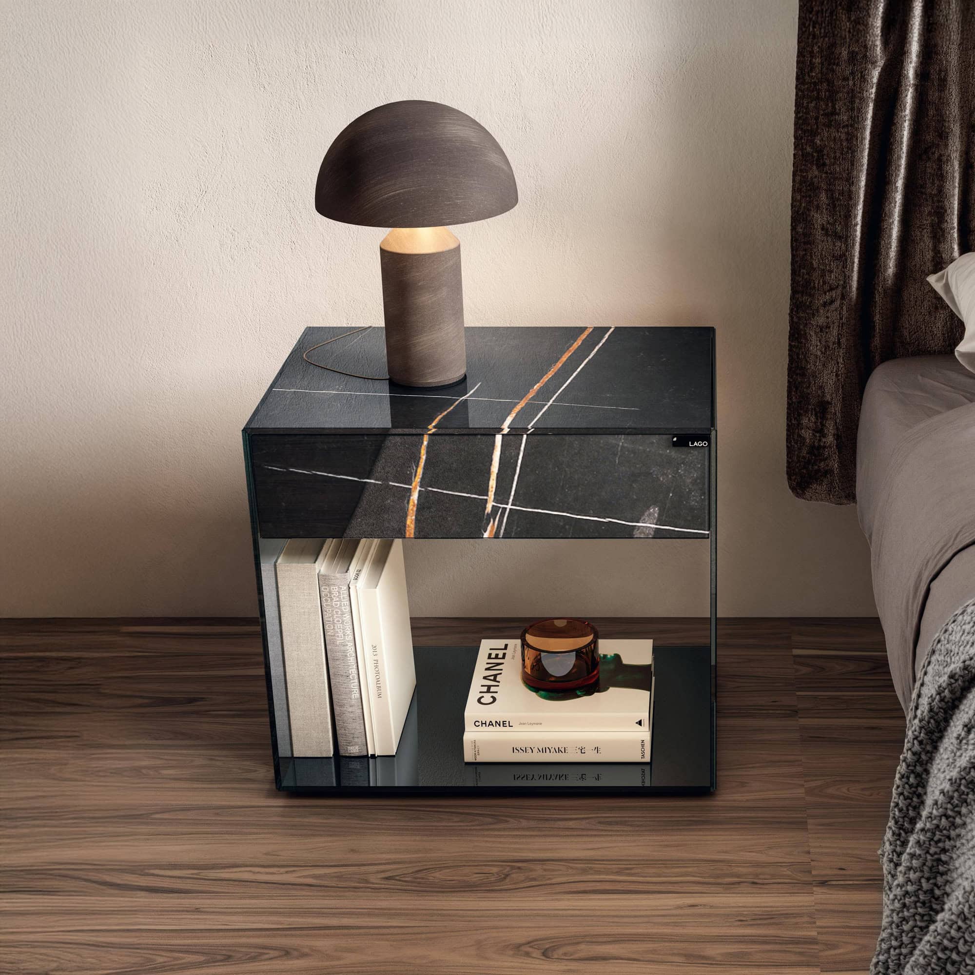 Lago UpGlass Bedside Table with transparent smoked glass design, styled beside a bed with a modern lamp on top.