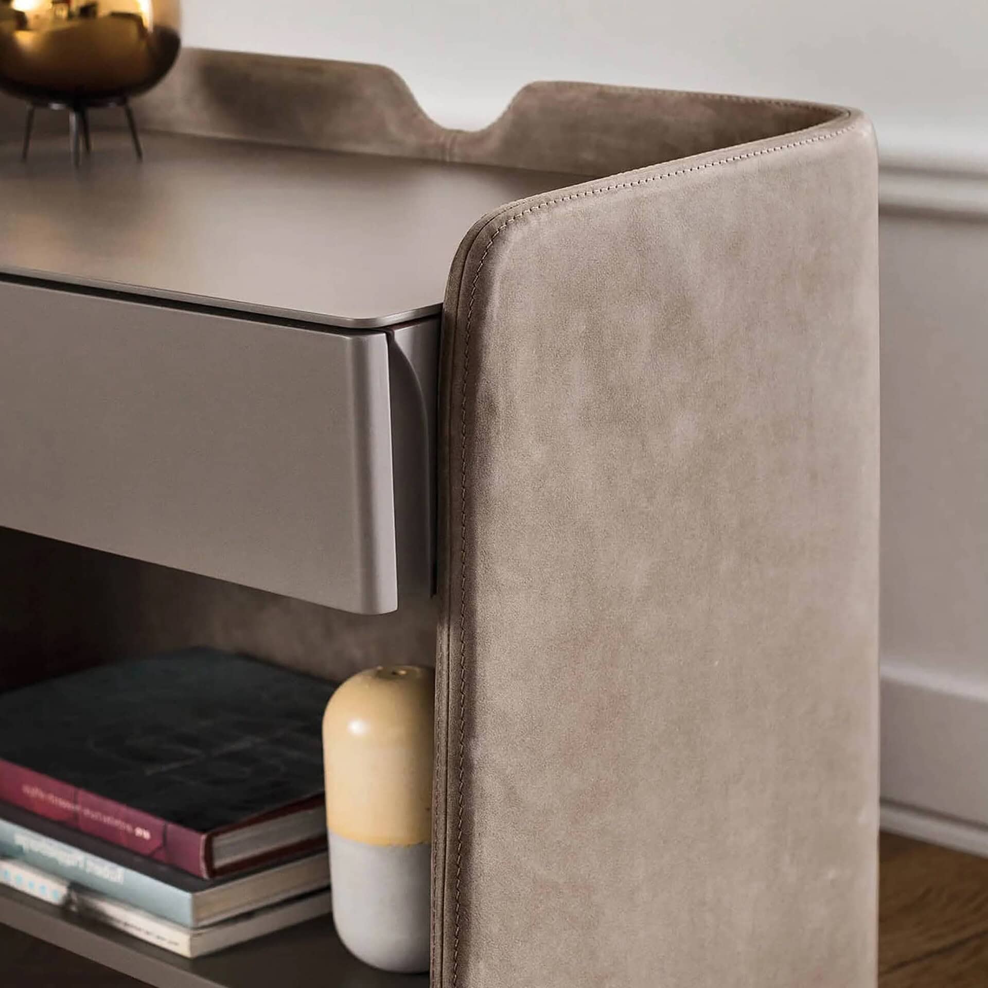 Close-up angled view of the Chloé Upholstered Nightstand in beige fabric with a matte lacquer drawer and open shelf below, styled with books and decor.
