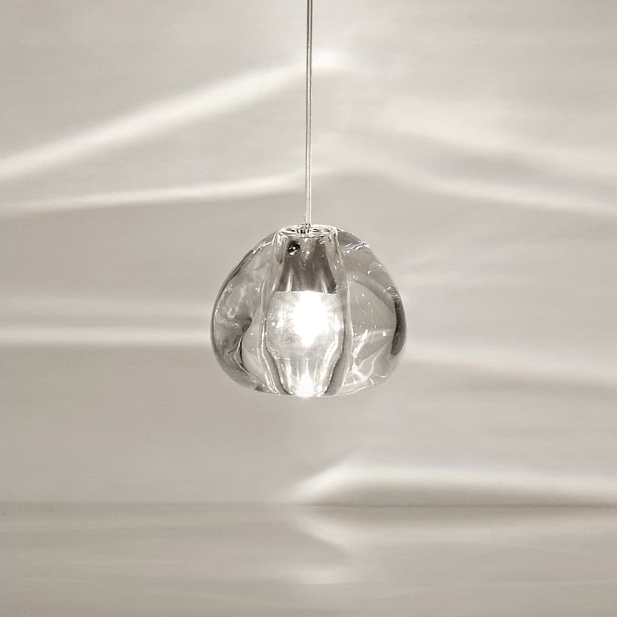 Close-up of the Terzani Mizu Pendant Light in clear crystal, casting water-like light reflections on the wall.