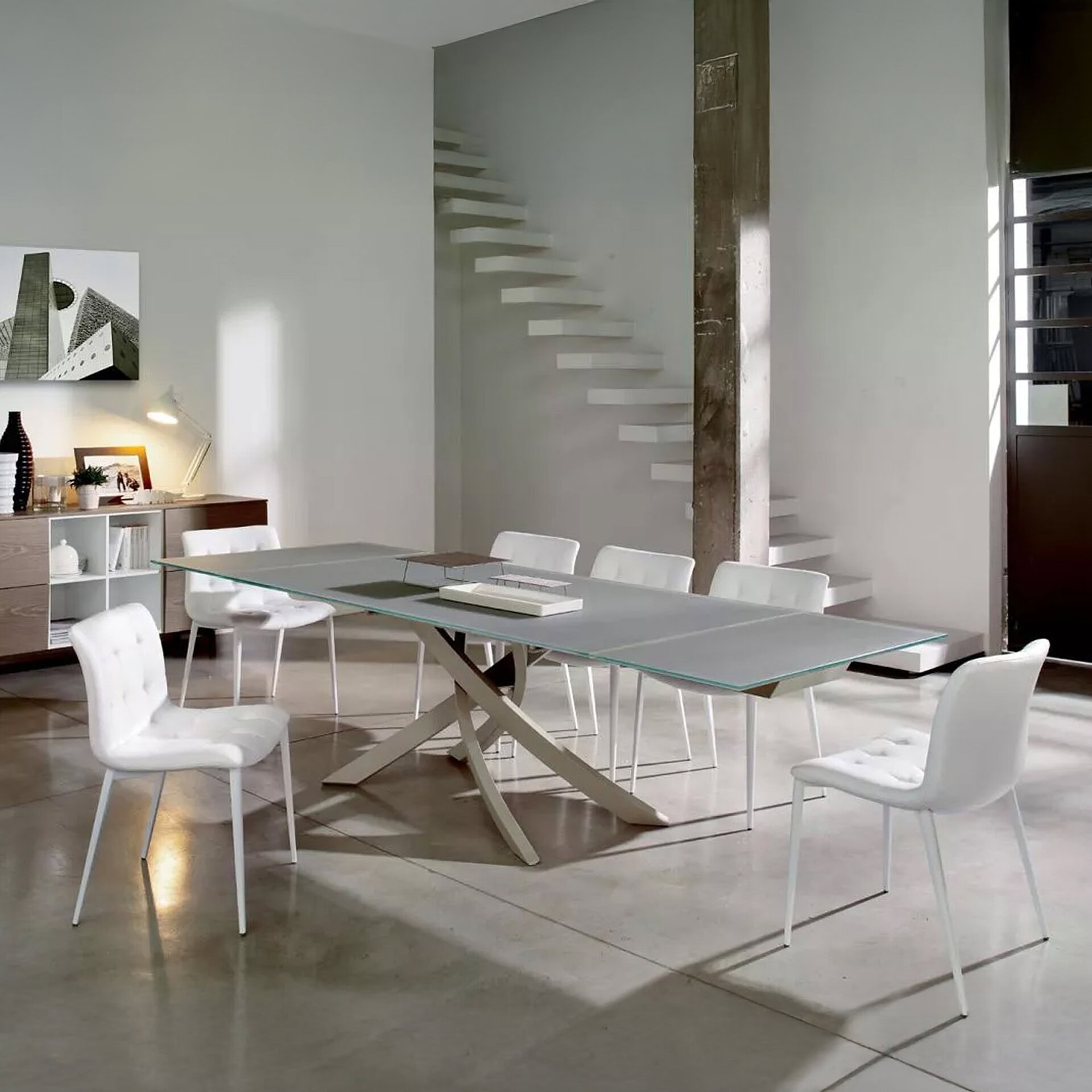 Modern Artistico extendable dining table in glass and metal base, displayed in a spacious open-plan home interior.