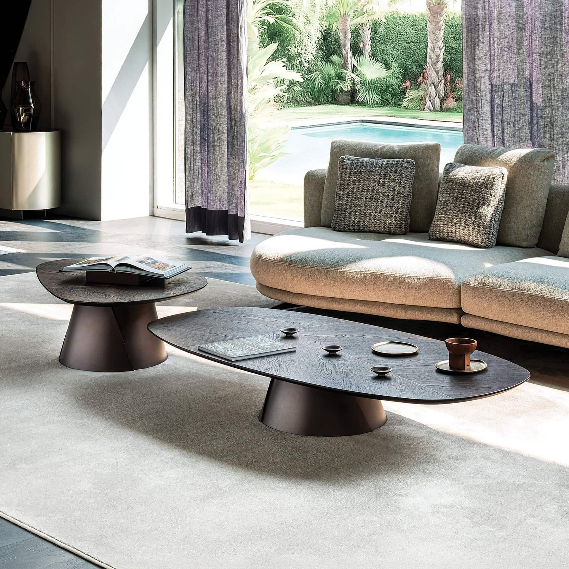 Modern living room with Sklar Furnishings coffee tables and plush sofa overlooking a backyard pool.