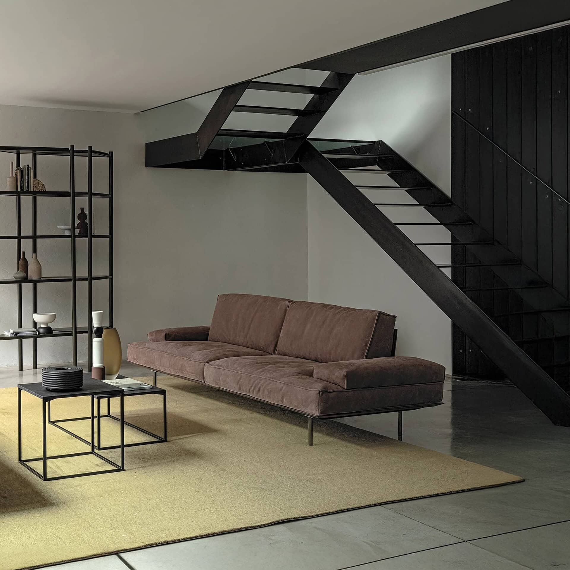 Sleek modern living room featuring contemporary sofa and stylish black staircase with minimalist decor.