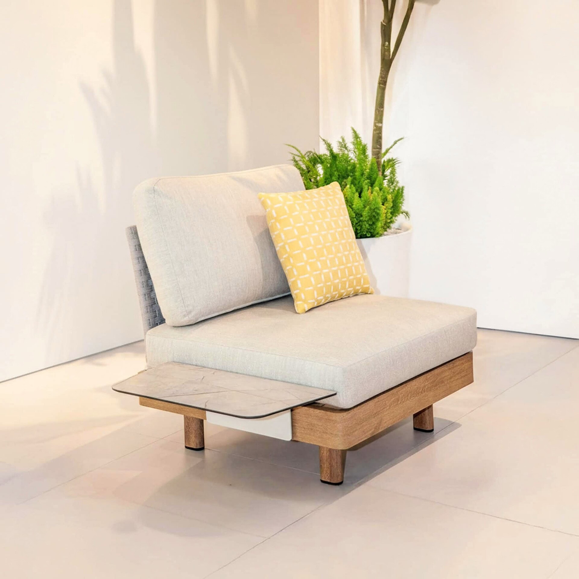 Modern beige outdoor sofa with wooden accents and a yellow patterned pillow.