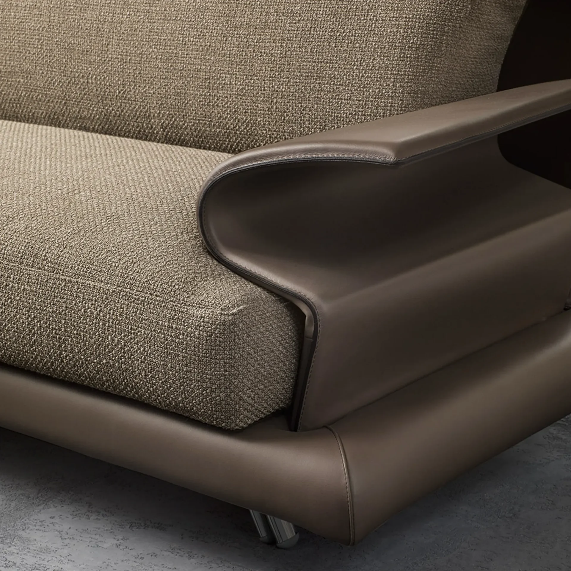 Close-up of a modern sofa featuring a curved dark brown leather armrest and light beige textured fabric cushions, highlighting the contrasting materials.