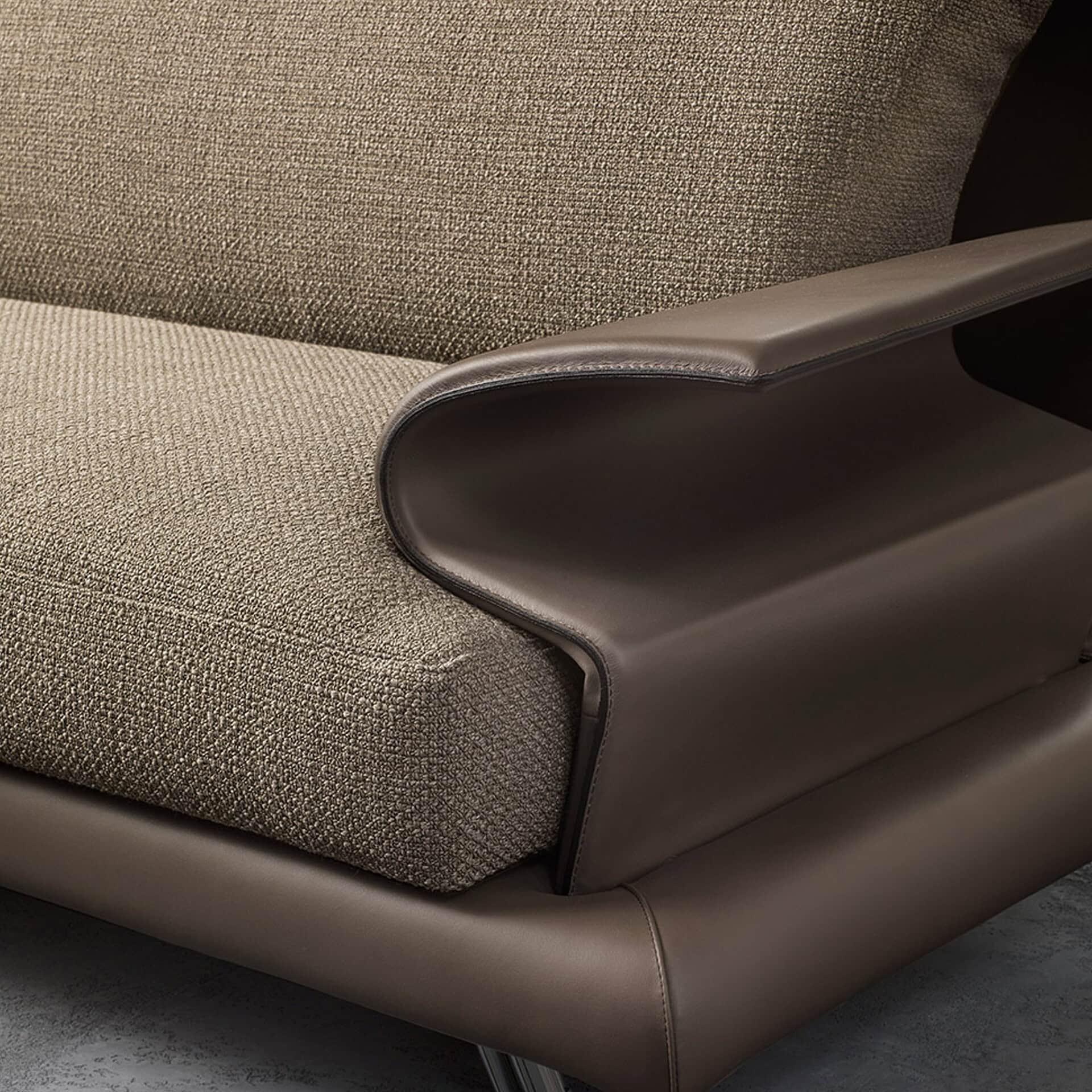 Close-up of a modern sofa featuring a curved dark brown leather armrest and light beige textured fabric cushions, highlighting the contrasting materials.