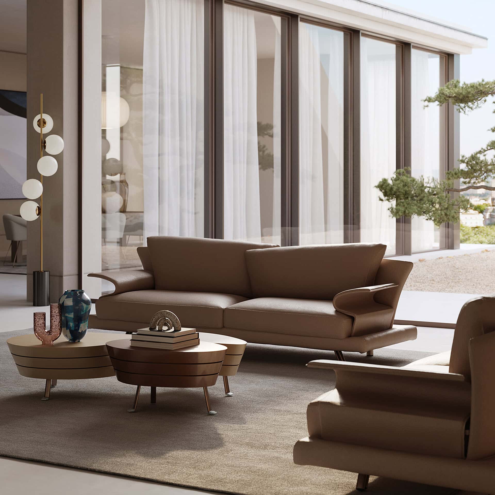 A modern living room with a brown leather sofa, two round coffee tables, and a tall floor lamp, set against a backdrop of large glass doors opening to an outdoor gravel area with a tree.
