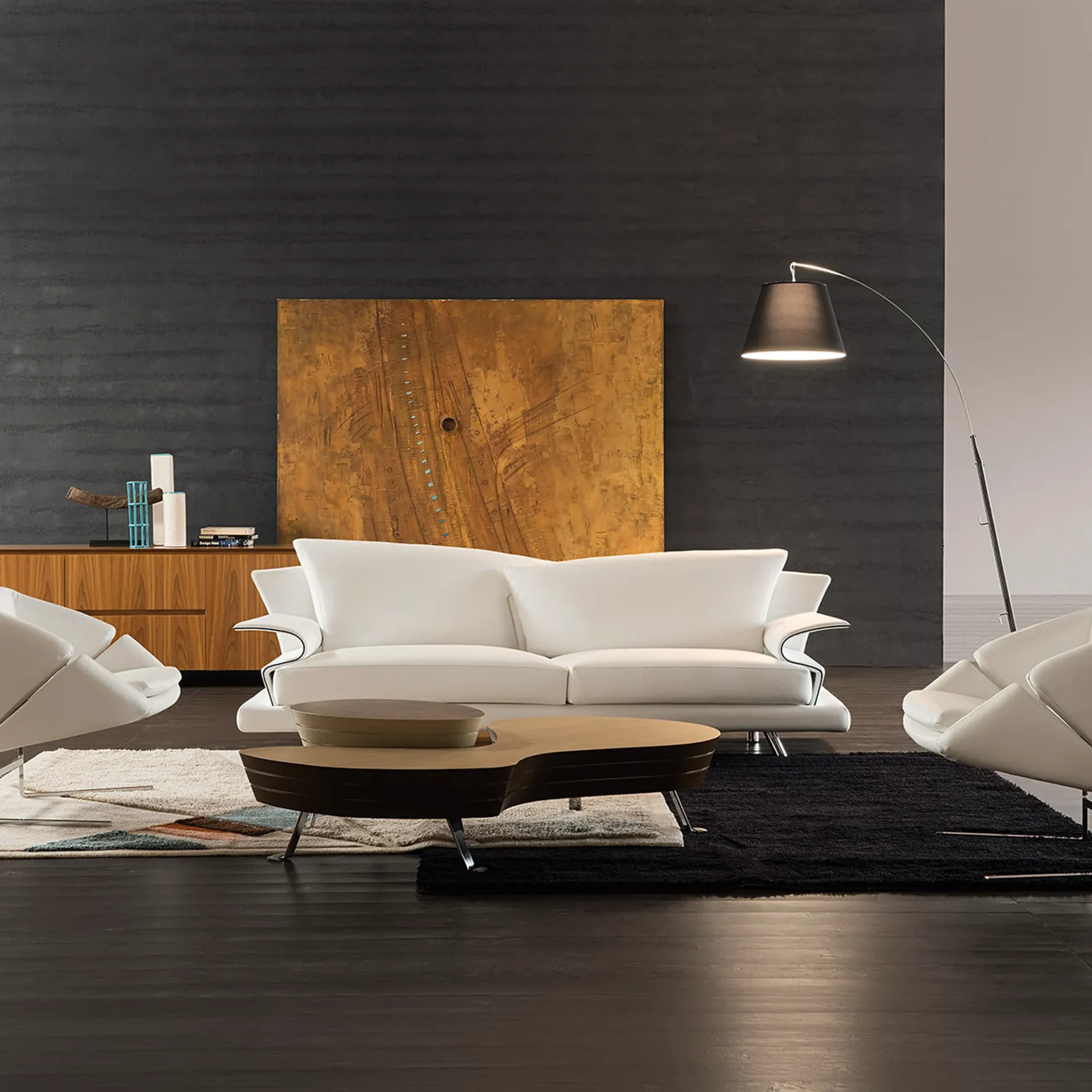 A modern living room with a white leather sofa, a unique two-tiered coffee table, and dark textured walls featuring a large abstract artwork and a wooden credenza. An arc floor lamp illuminates the scene.